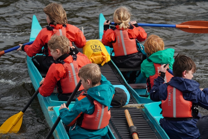 Photo of the backs of a group of children paddling a group kayak