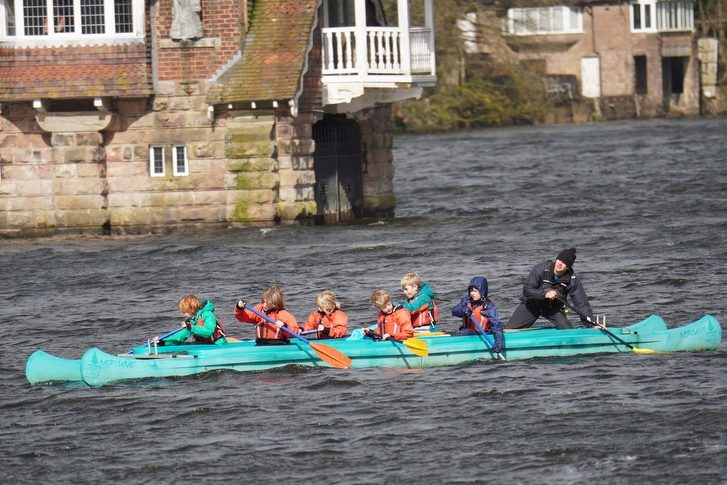 Large group of children in a large kayak with a instructor at the back