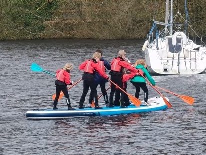 Group of children stood up on a large Stand Up Paddleboard on a lake