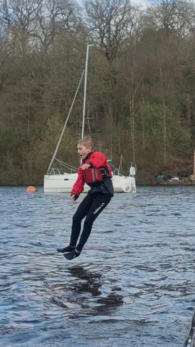 Child in a wetsuit jumping into a lake